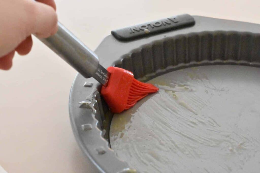 Greasing the tart pan with a silicone brush and melted butter.
