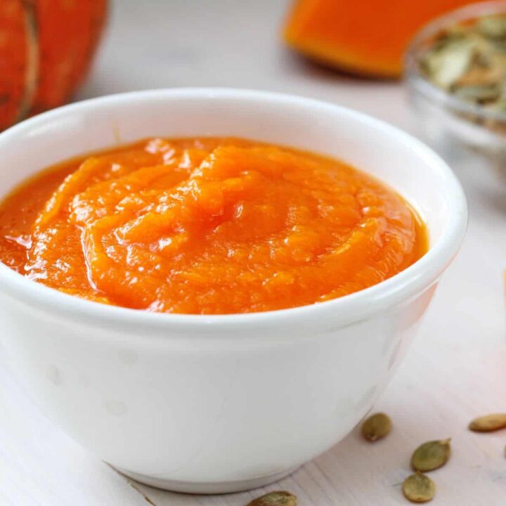 Bowl of pumpkin puree next to pumpkin wedges.